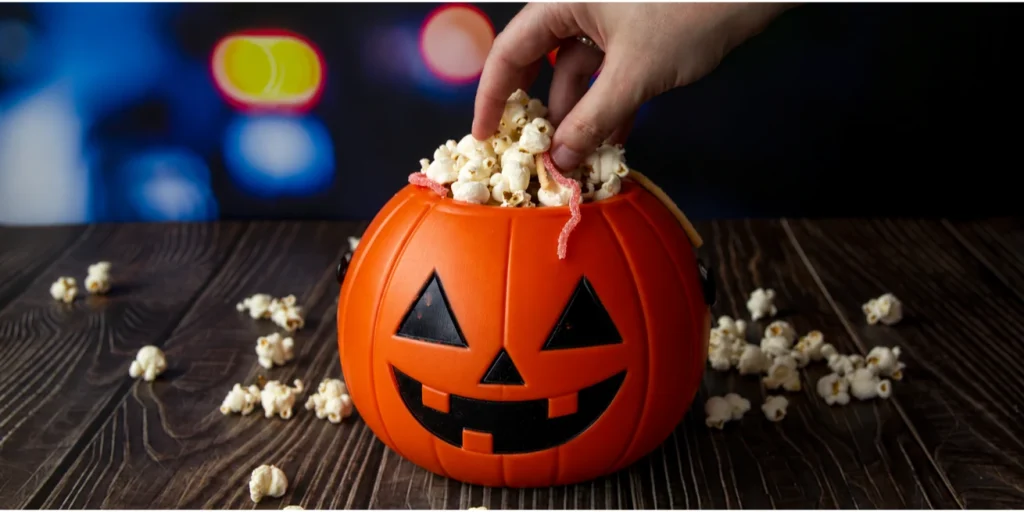 A hand reaching into a jack-o’-lantern bucket full of popcorn