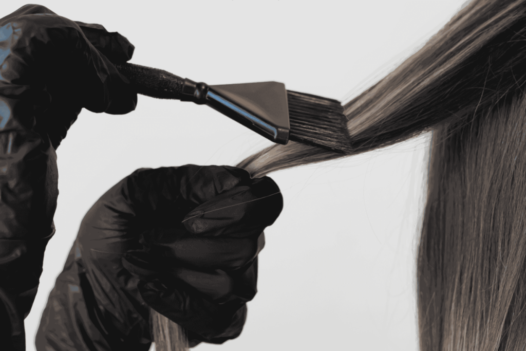 Stylist in black gloves brushing colour onto a section of long hair